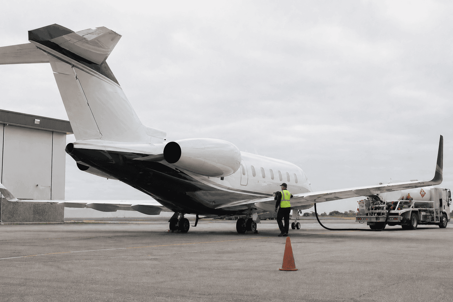 Super-midsize business jet being refueled on the apron, with ground crew and fuel truck in operation