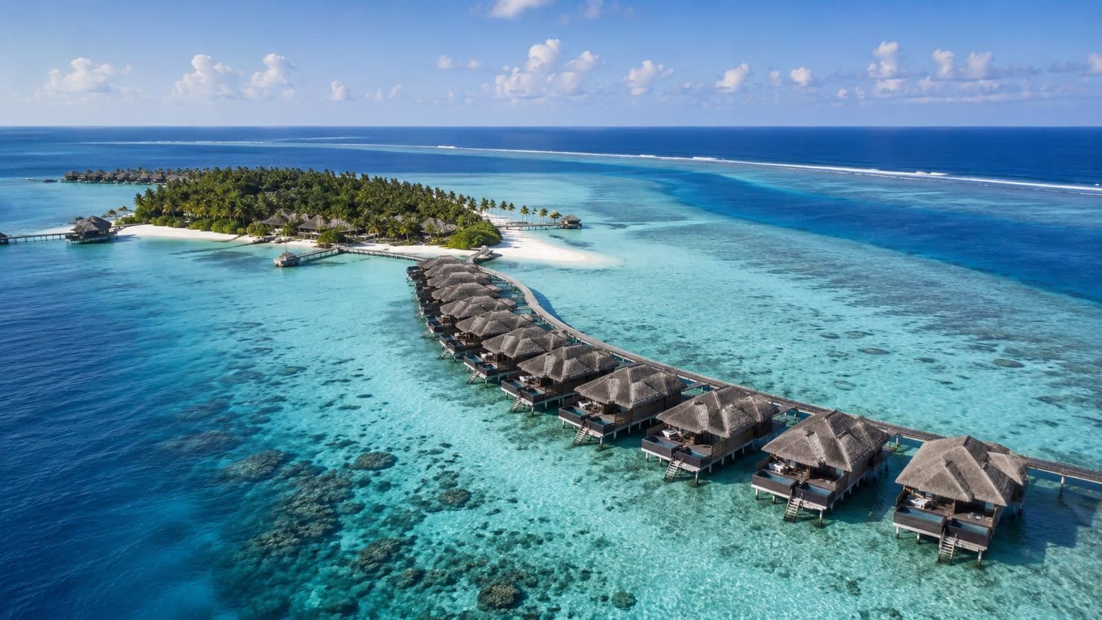 Aerial view of a luxury Maldives island resort with overwater villas, white sand beaches, and crystal-clear turquoise lagoons.