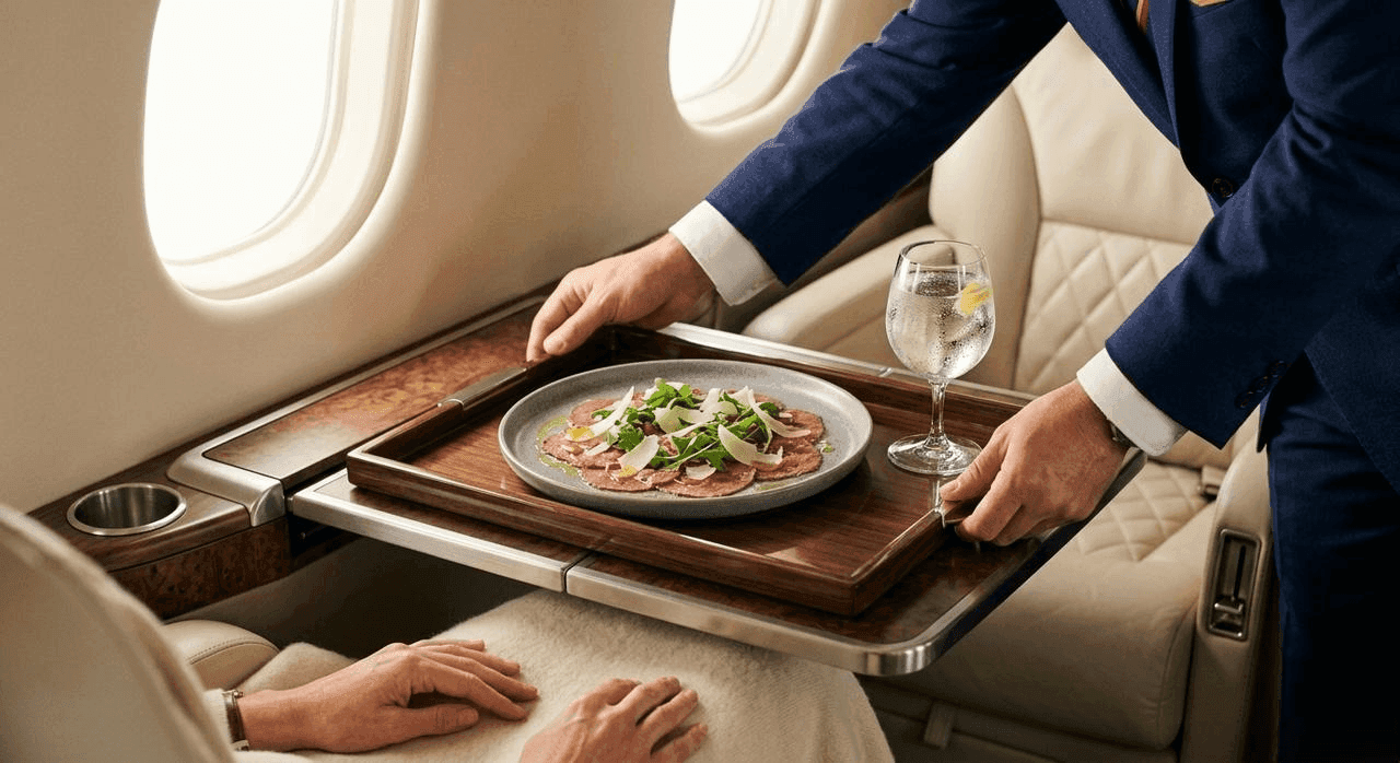 Flight attendant serving a gourmet dish to a passenger in a luxury business jet cabin.
