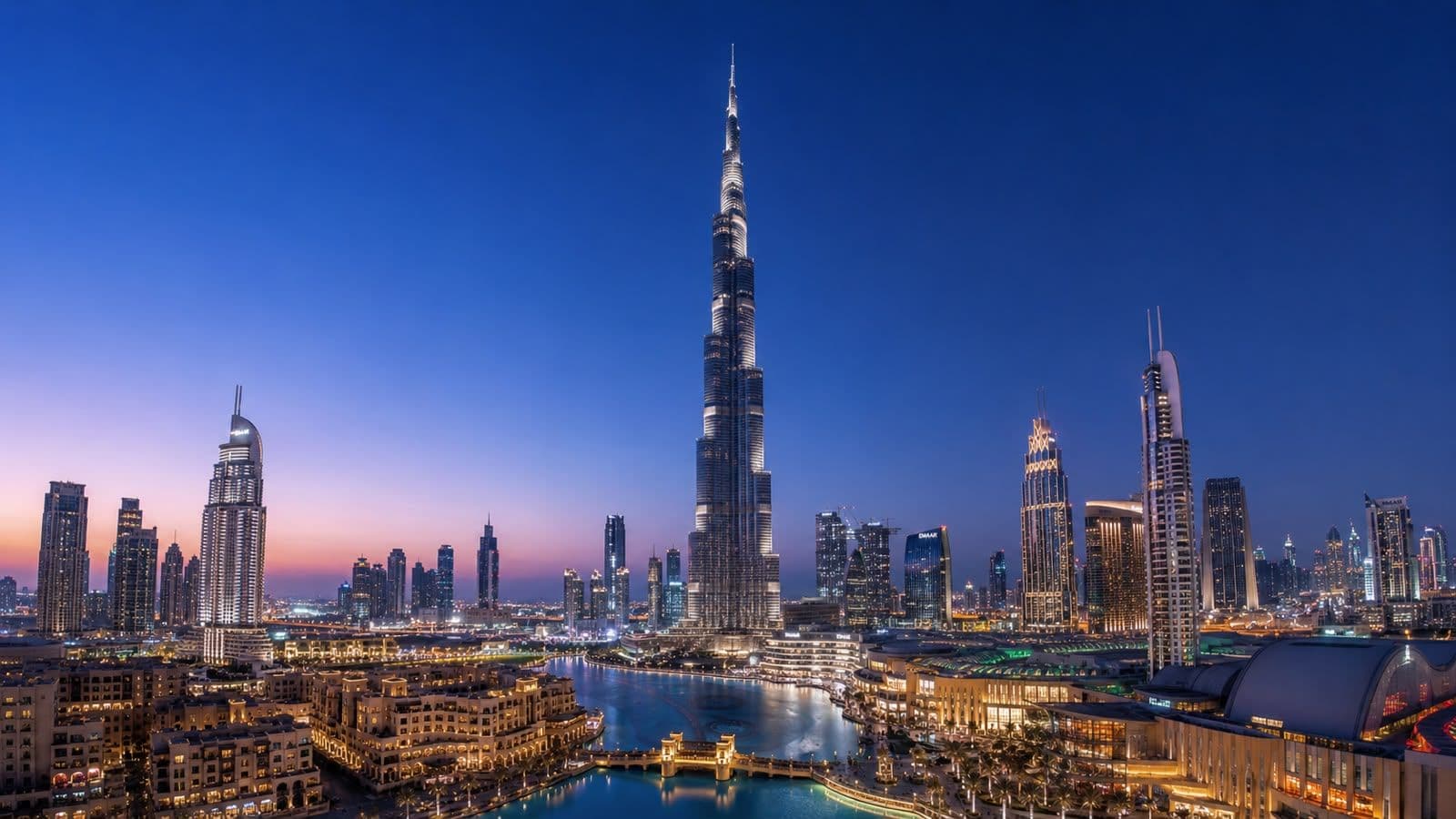 Panoramic view of Dubai skyline at dusk featuring the Burj Khalifa towering above the city's illuminated skyscrapers and waterfront.