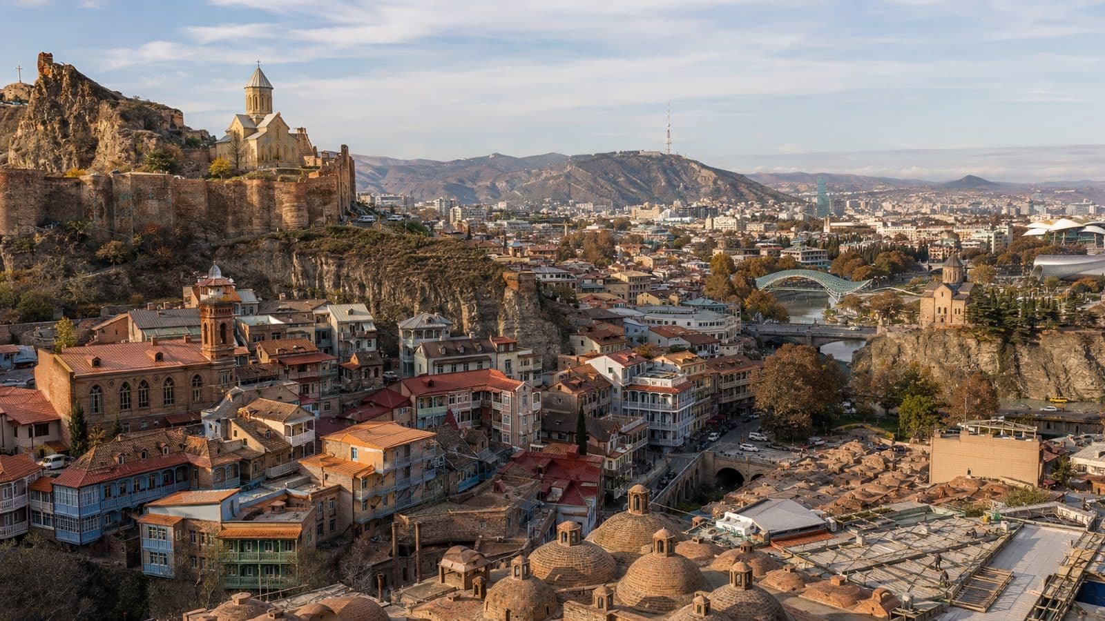 Panoramic view of Tbilisi’s Old Town, Narikala Fortress, historic churches, sulfur bath domes, and the Kura River with the Peace Bridge in the background.