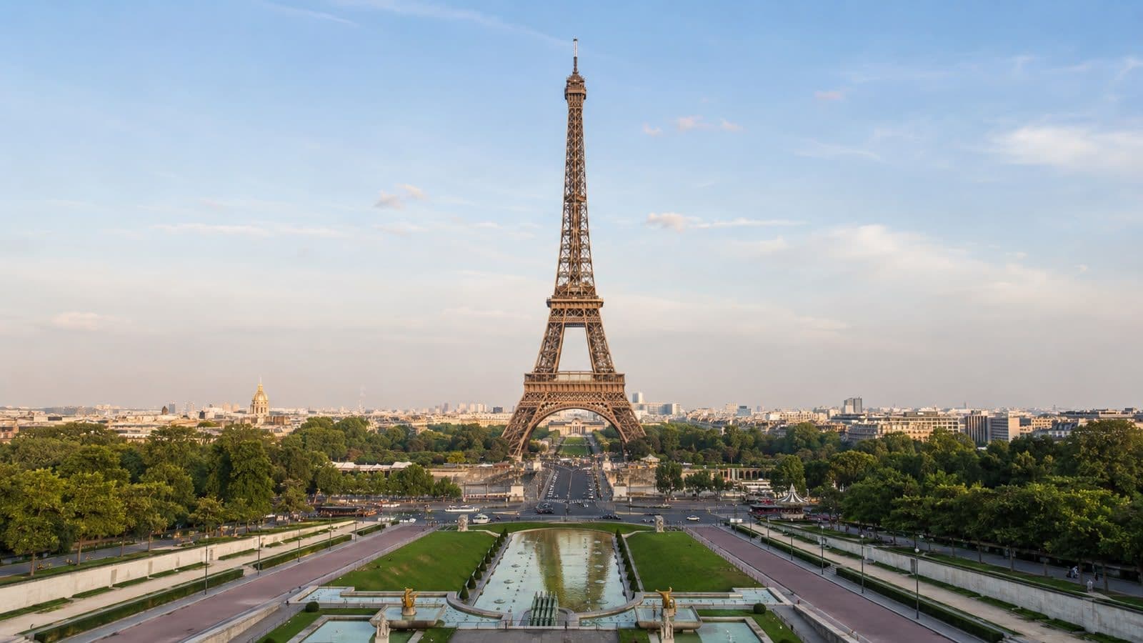 Panoramic view of the Eiffel Tower in Paris, framed by the Trocadéro Gardens and reflecting pools beneath a clear blue sky.