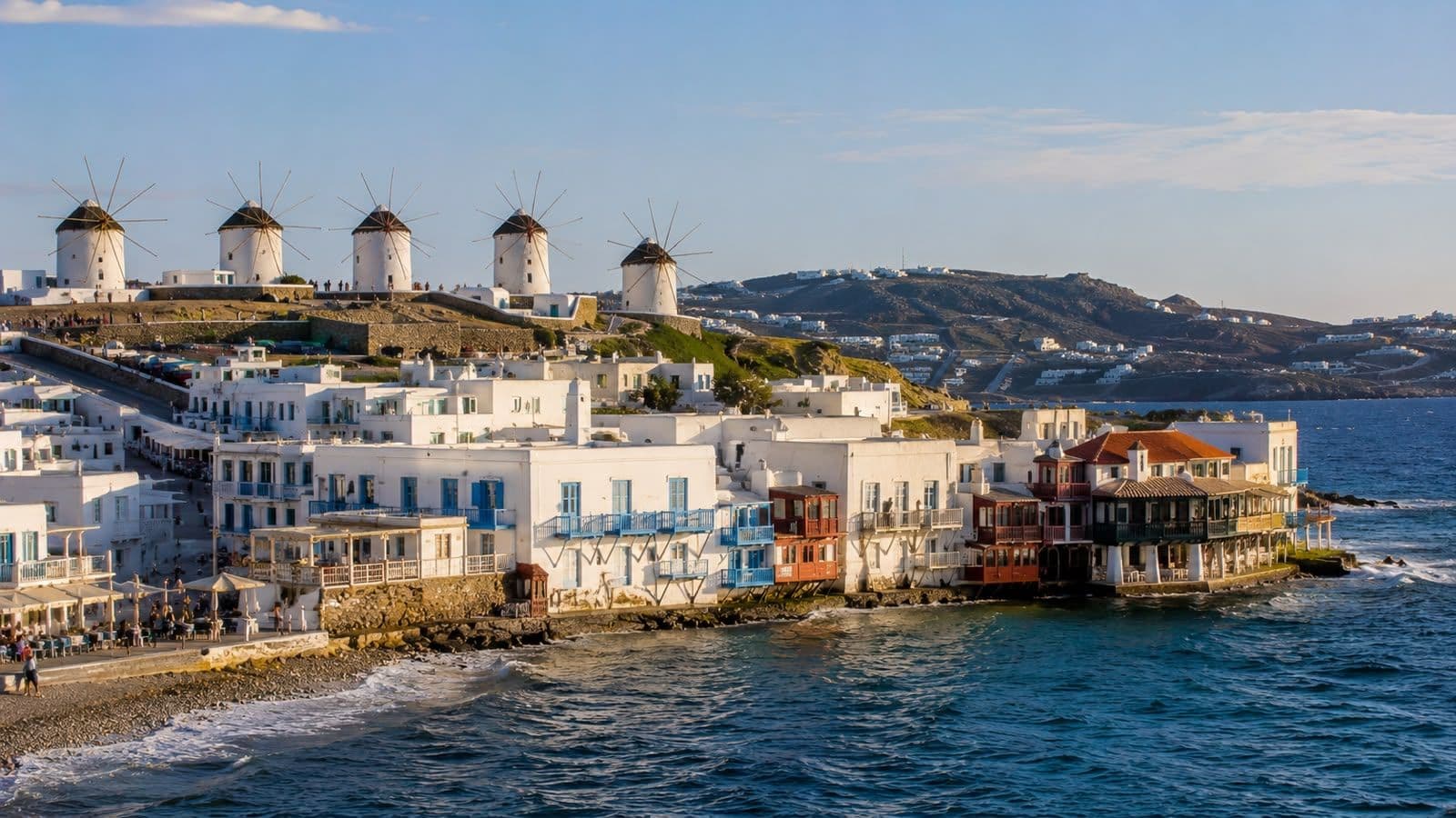 Panoramic view of Mykonos’ iconic windmills, whitewashed waterfront houses, and Aegean Sea coastline.
